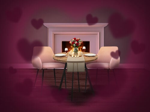 Mise en sc&egrave;ne romantique avec une petite table ronde dress&eacute;e pour deux, des chaises rembourr&eacute;es roses, des bougies et un bouquet de roses, plac&eacute;e devant une chemin&eacute;e allum&eacute;e, avec des formes de c&oelig;urs douces cr&eacute;ant une ambiance de Saint-Valentin. Cliquez pour voir les articles en promotion