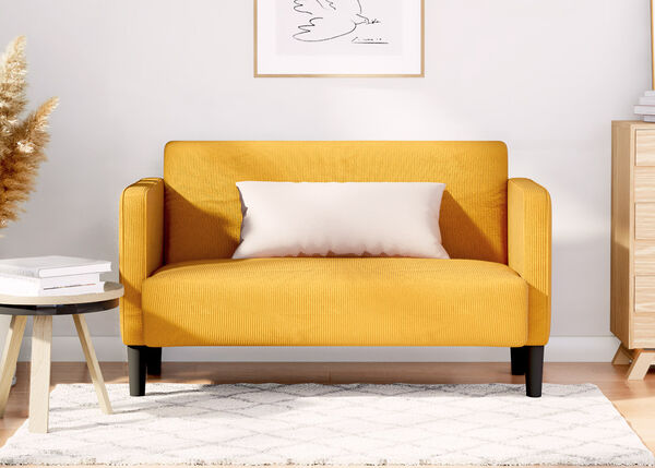 Canap&eacute; deux places jaune avec coussin blanc, &agrave; c&ocirc;t&eacute; d'une table d'appoint en bois et d'une commode en bois, sur un tapis &agrave; motifs dans un salon styl&eacute;.