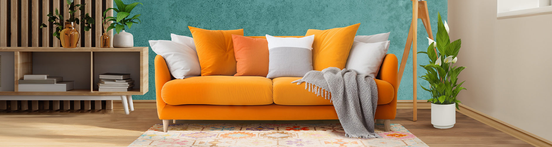 Un salon moderne avec un canapé moelleux orange décoré de coussins orange et blancs et d’un plaid gris, une plante verte à côté, ainsi qu’un meuble TV à étagères ouvertes contenant des livres et surmonté d’une autre plante verte.